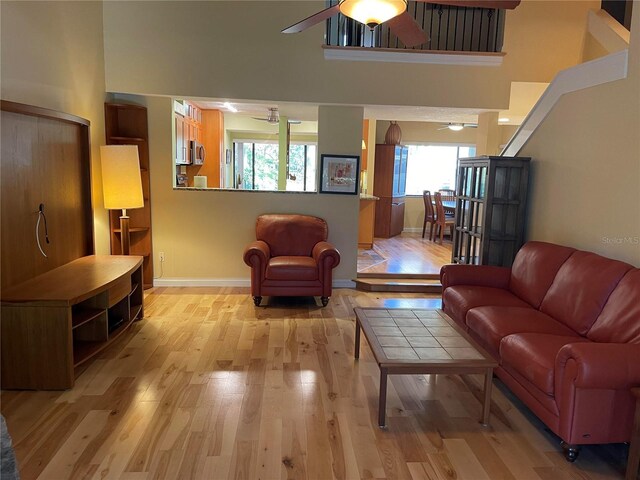 living room featuring a towering ceiling, ceiling fan, and light wood-type flooring