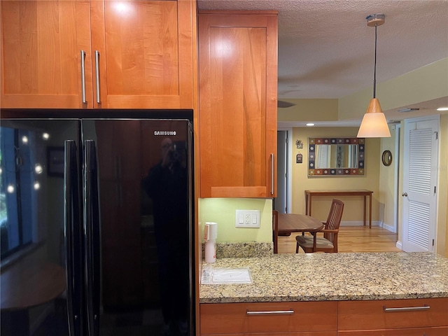 kitchen with brown cabinets, freestanding refrigerator, decorative light fixtures, and light stone countertops