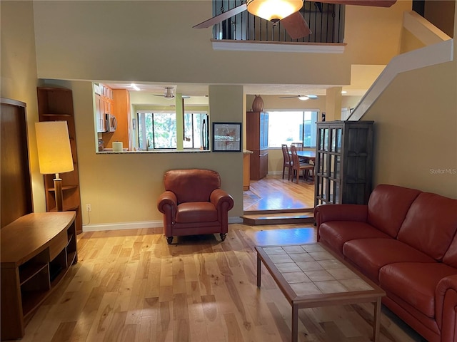 living room with light wood finished floors, ceiling fan, a high ceiling, and baseboards