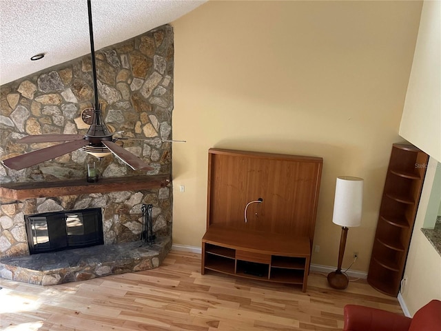 interior space with a textured ceiling, ceiling fan, a stone fireplace, wood finished floors, and baseboards