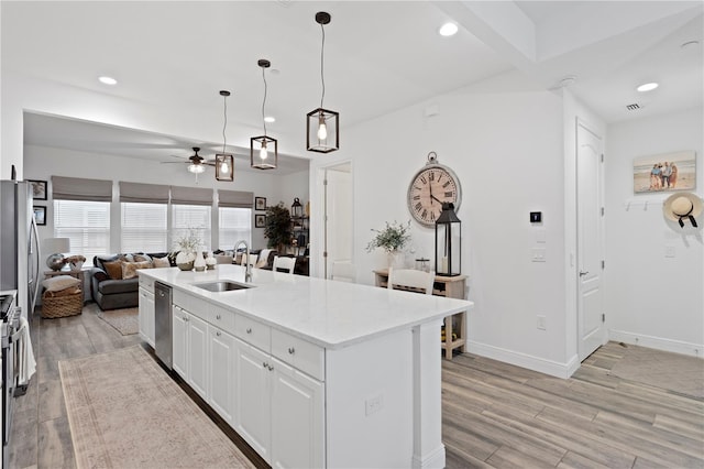 kitchen featuring hanging light fixtures, sink, white cabinets, stainless steel appliances, and a center island with sink