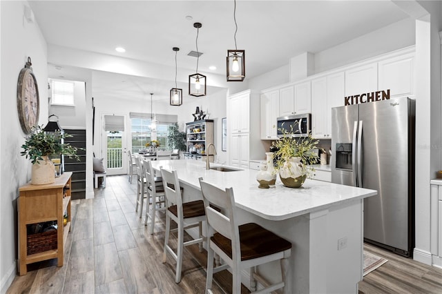 kitchen with hanging light fixtures, a large island, sink, white cabinets, and stainless steel appliances