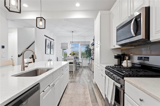 kitchen with sink, stainless steel appliances, white cabinetry, and hanging light fixtures