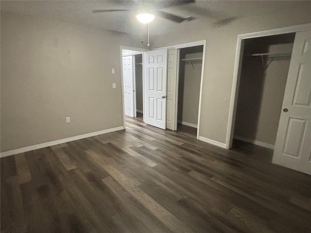 unfurnished bedroom with ceiling fan, dark hardwood / wood-style flooring, and multiple closets