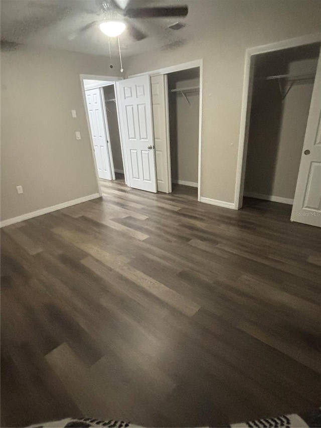 unfurnished bedroom featuring ceiling fan, dark hardwood / wood-style floors, and multiple closets