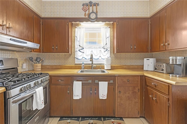 kitchen with light tile patterned floors, decorative backsplash, stainless steel gas stove, and sink