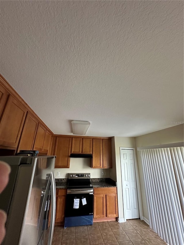 kitchen featuring a textured ceiling, electric range, stainless steel fridge, and tile patterned floors