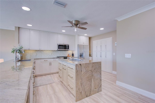 kitchen featuring appliances with stainless steel finishes, sink, white cabinets, a center island, and light stone counters