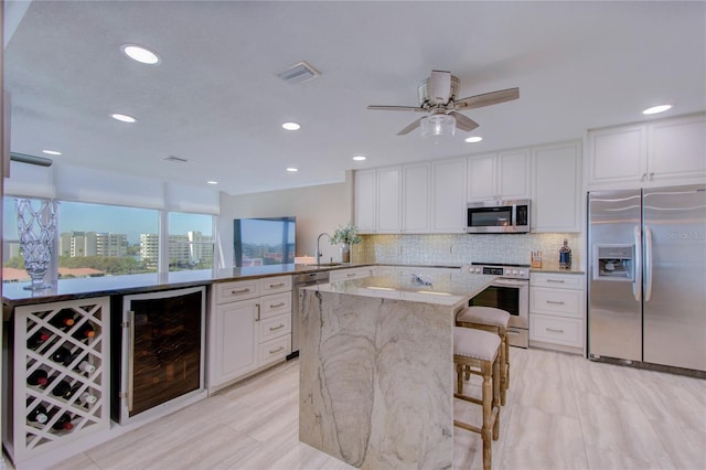 kitchen featuring a kitchen bar, white cabinetry, appliances with stainless steel finishes, kitchen peninsula, and beverage cooler