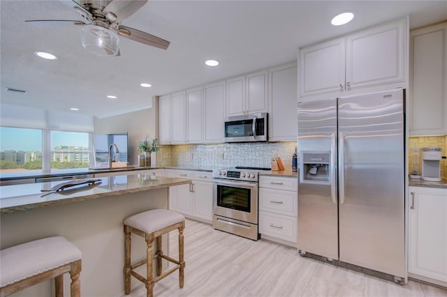 kitchen with white cabinetry, light stone countertops, a breakfast bar area, and stainless steel appliances