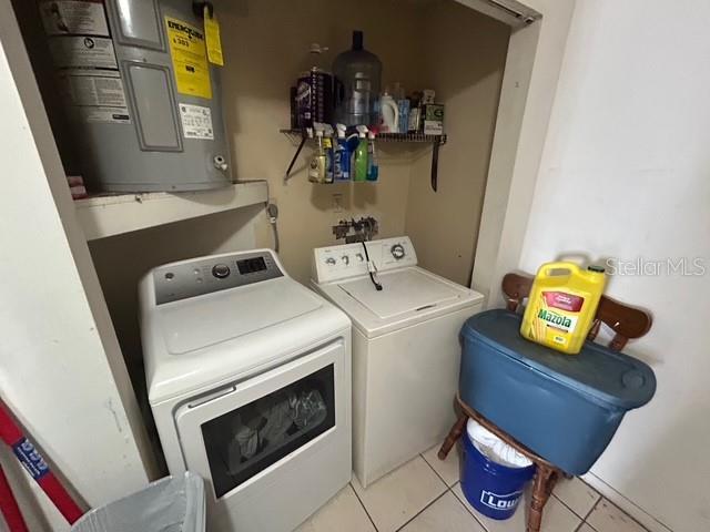 laundry room with electric water heater, washing machine and dryer, and light tile patterned floors