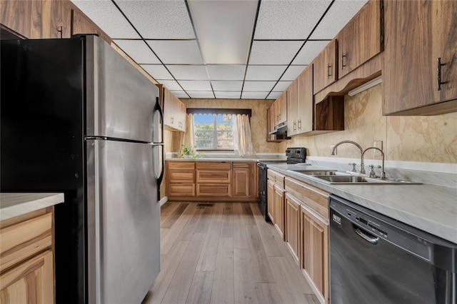 kitchen featuring black appliances, a drop ceiling, light hardwood / wood-style flooring, and sink