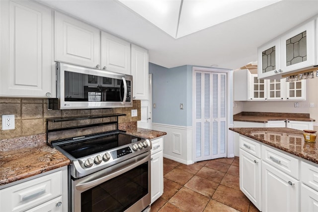 kitchen with appliances with stainless steel finishes, white cabinetry, dark stone counters, decorative backsplash, and light tile patterned floors