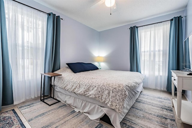 bedroom featuring ceiling fan, light tile patterned floors, and a textured ceiling