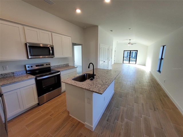 kitchen with white cabinetry, lofted ceiling, sink, stainless steel appliances, and a center island with sink