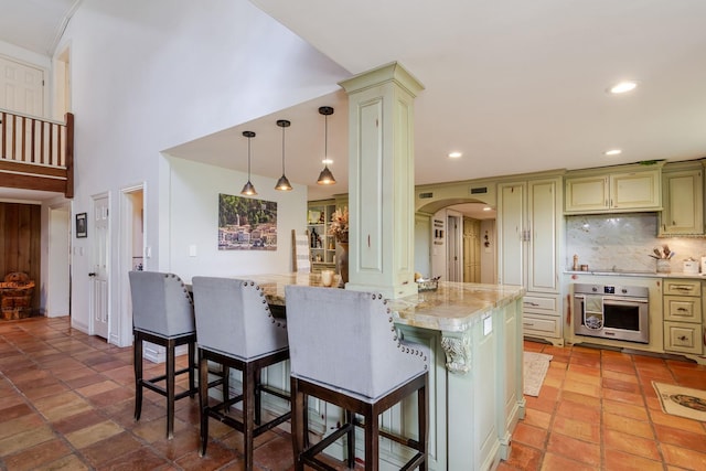 kitchen featuring tasteful backsplash, a breakfast bar area, stainless steel oven, kitchen peninsula, and light stone countertops