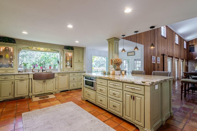 kitchen featuring sink, dishwasher, hanging light fixtures, wooden walls, and a center island