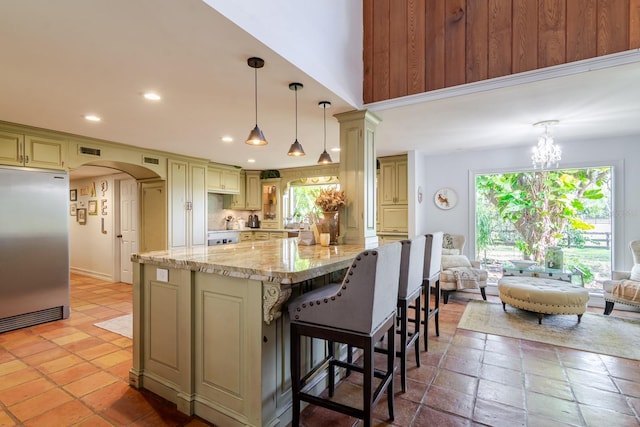 kitchen with hanging light fixtures, a center island, light stone counters, cream cabinetry, and built in fridge