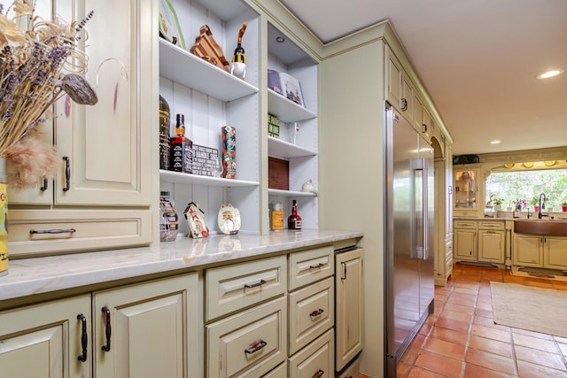 bar featuring sink, light tile patterned floors, cream cabinets, high quality fridge, and light stone countertops