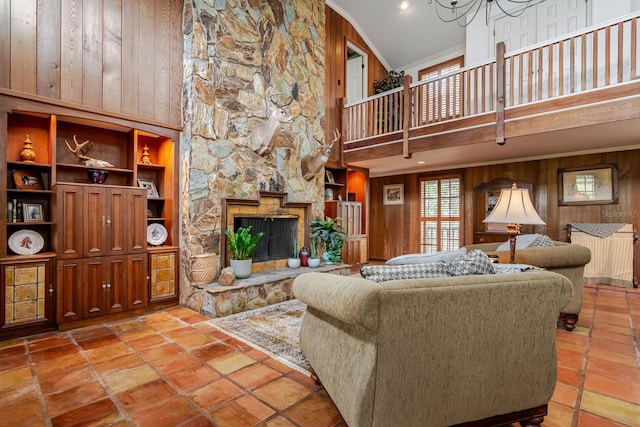 tiled living room with crown molding, wooden walls, a stone fireplace, and a high ceiling