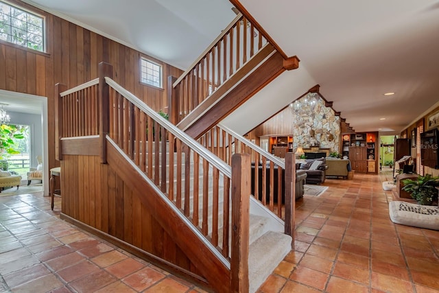 stairs featuring wood walls, crown molding, a chandelier, vaulted ceiling, and a fireplace