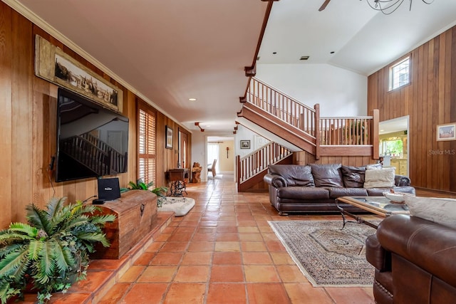 tiled living room with lofted ceiling, ornamental molding, ceiling fan, and wood walls