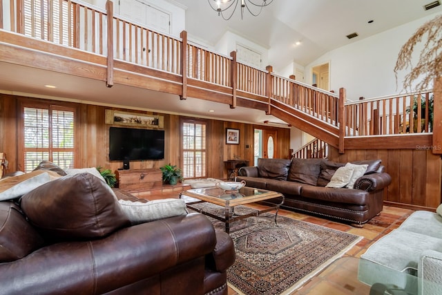 living room with light tile patterned floors, a towering ceiling, a chandelier, and wood walls