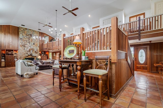 dining room with ceiling fan with notable chandelier, high vaulted ceiling, and wood walls