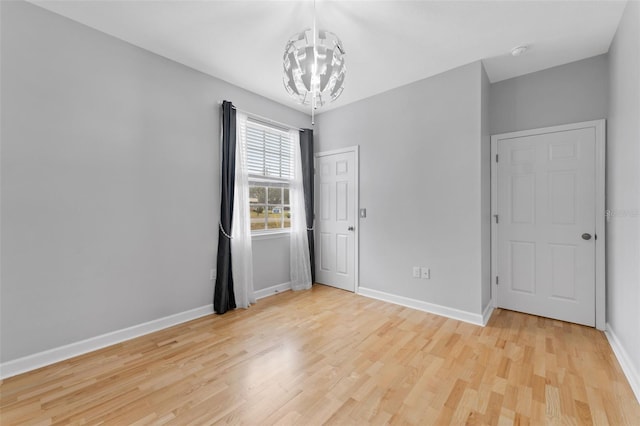 spare room featuring light wood finished floors, baseboards, and a notable chandelier