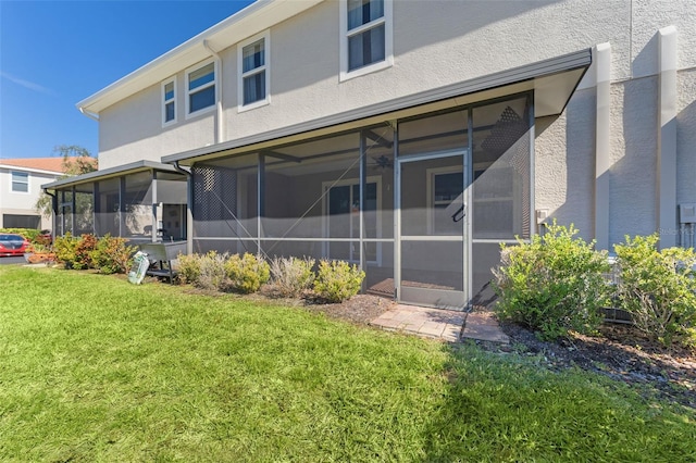 rear view of property featuring a yard, a sunroom, and stucco siding