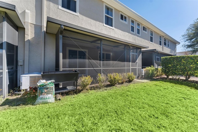 rear view of house with a sunroom, a lawn, central AC unit, and stucco siding