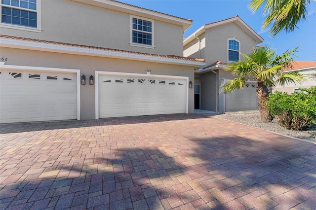 view of front of home with decorative driveway, a tiled roof, an attached garage, and stucco siding