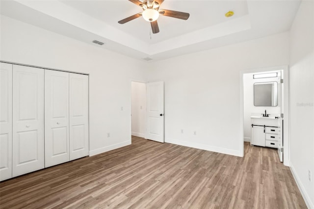 unfurnished bedroom with ceiling fan, a raised ceiling, light hardwood / wood-style floors, and a closet