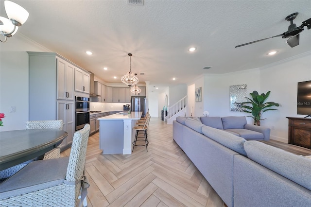 living room with ornamental molding, light parquet flooring, ceiling fan with notable chandelier, and a textured ceiling