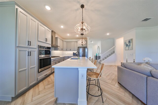 kitchen with hanging light fixtures, an island with sink, light parquet flooring, and appliances with stainless steel finishes