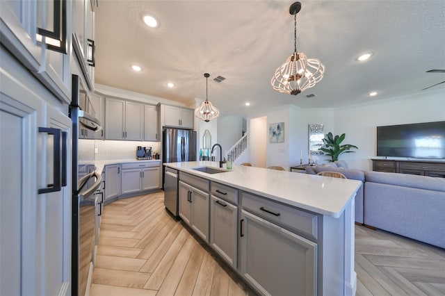 kitchen with sink, stainless steel appliances, a center island with sink, decorative light fixtures, and light parquet flooring