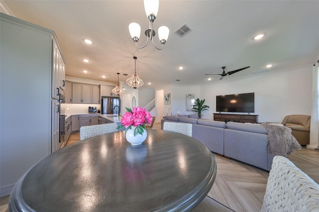 dining space with light parquet floors, sink, and ceiling fan with notable chandelier