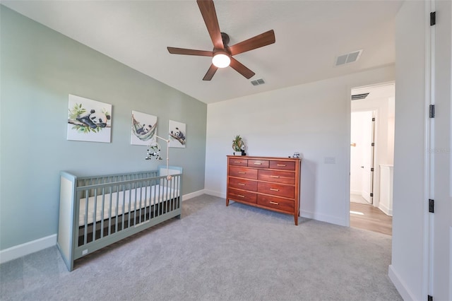 carpeted bedroom with a crib and ceiling fan