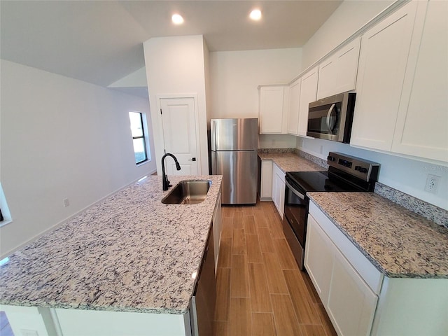 kitchen featuring sink, appliances with stainless steel finishes, white cabinetry, light stone countertops, and an island with sink