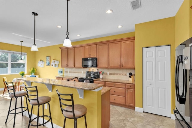 kitchen with pendant lighting, a kitchen bar, a kitchen island with sink, black appliances, and light stone countertops