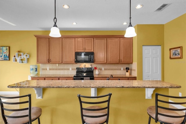 kitchen with a kitchen bar, tasteful backsplash, black appliances, a kitchen island, and decorative light fixtures