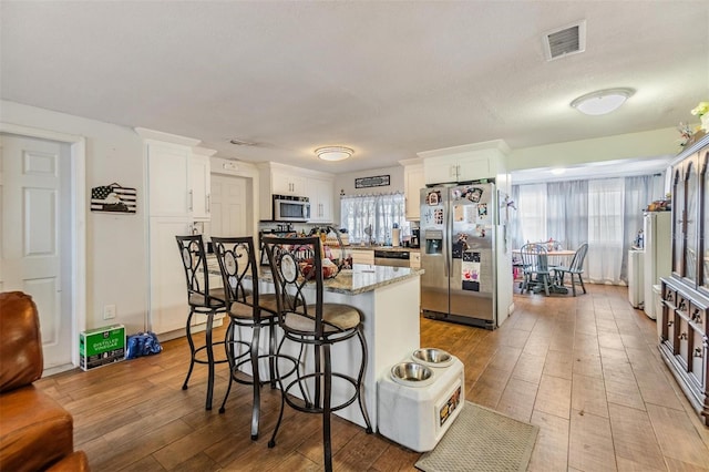 kitchen featuring light stone countertops, white cabinets, a kitchen bar, stainless steel appliances, and light hardwood / wood-style floors