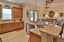 kitchen with a kitchen bar, sink, decorative light fixtures, stainless steel dishwasher, and light stone countertops