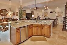 kitchen featuring stainless steel dishwasher, decorative light fixtures, light stone countertops, and a center island with sink