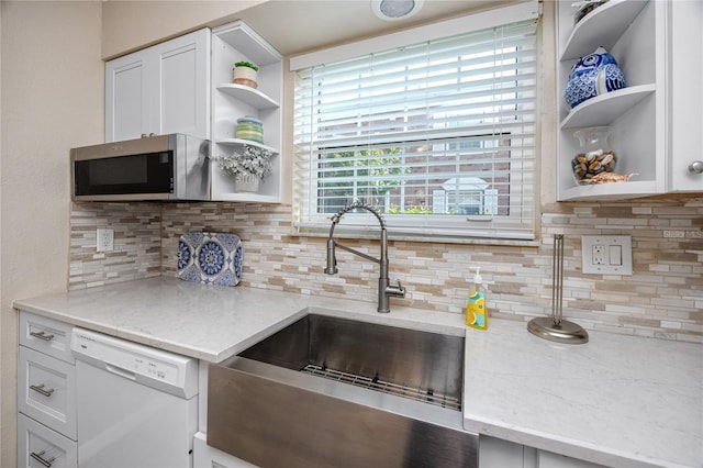 kitchen with white dishwasher, sink, backsplash, white cabinetry, and light stone countertops