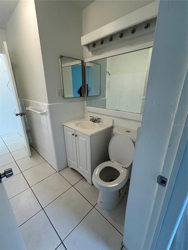 bathroom with toilet, vanity, tile patterned floors, and tile walls