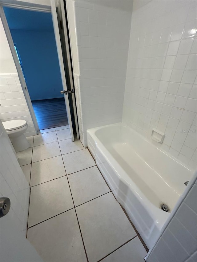 bathroom featuring toilet, tile patterned floors, a bath, and tile walls