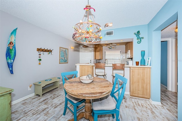 dining space featuring ceiling fan, sink, a textured ceiling, and light wood-type flooring