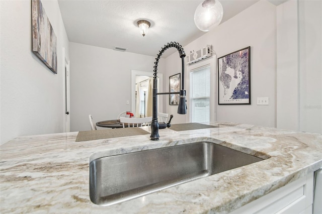 kitchen with light stone counters, sink, a textured ceiling, and white cabinets