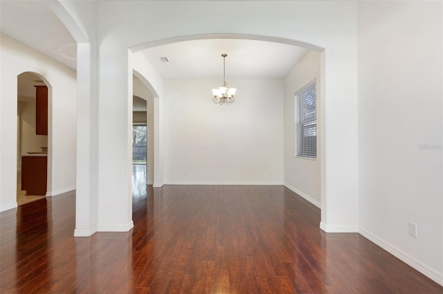 spare room featuring dark wood-type flooring and an inviting chandelier